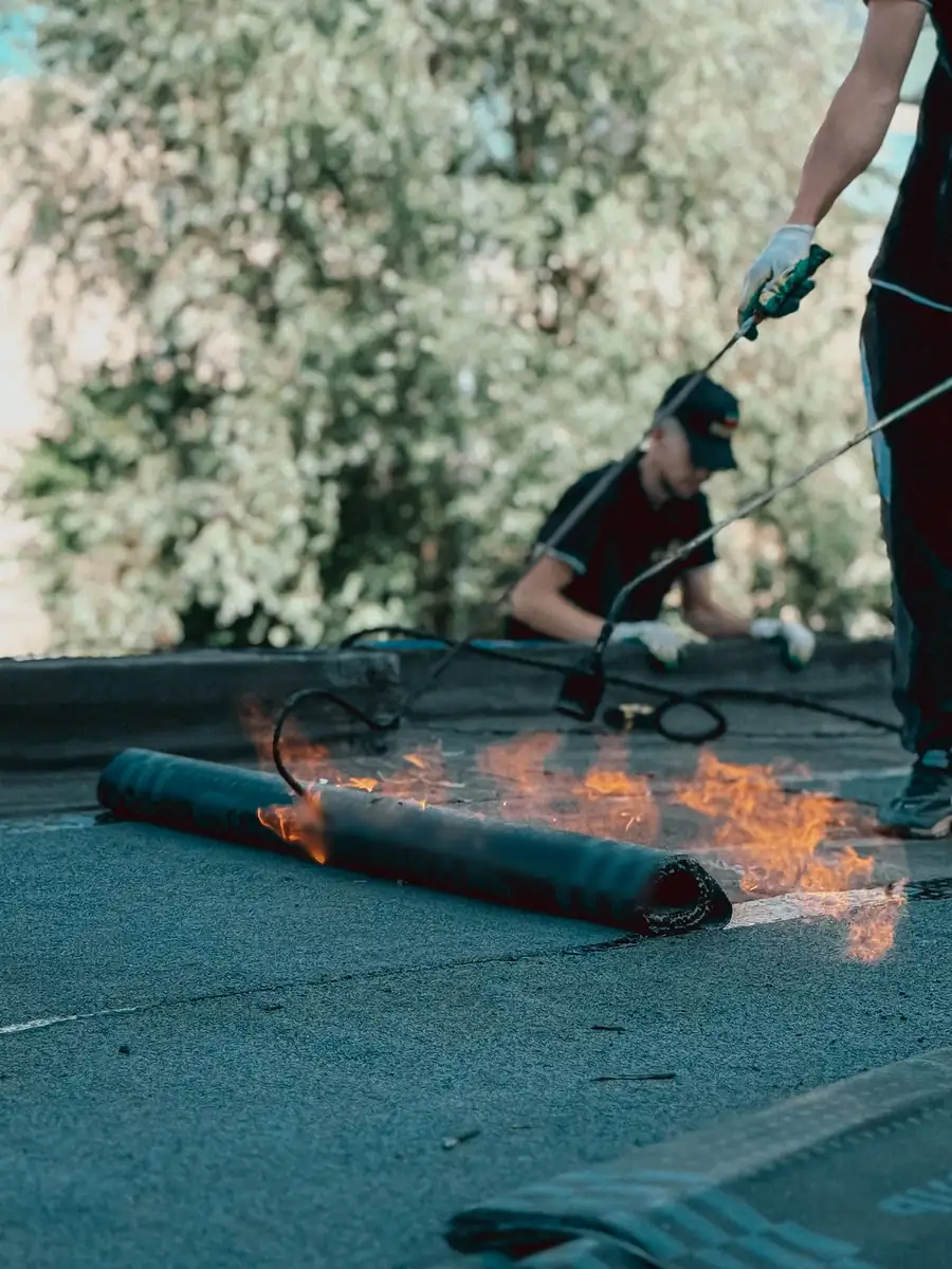 Roofers torching down a rubber membrane on a flat roof, with flames running along the seam