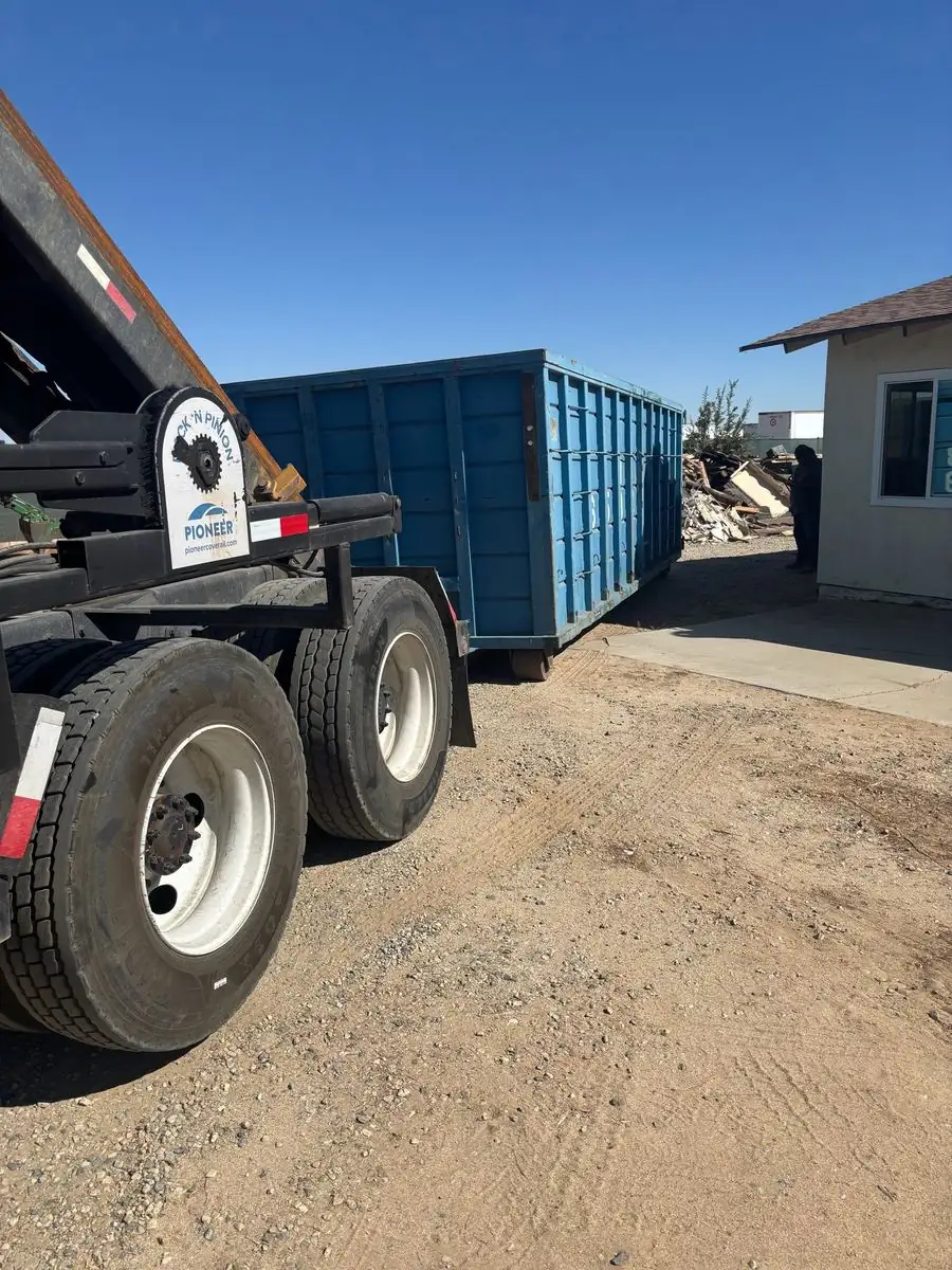 Roll-off truck parked beside a blue roll-off dumpster in a dirt yard
